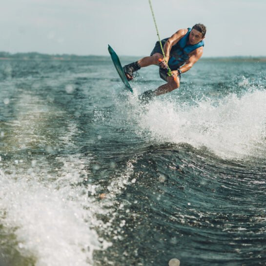 young man doing wakeboarding in a lake whit mountains also doing jumps